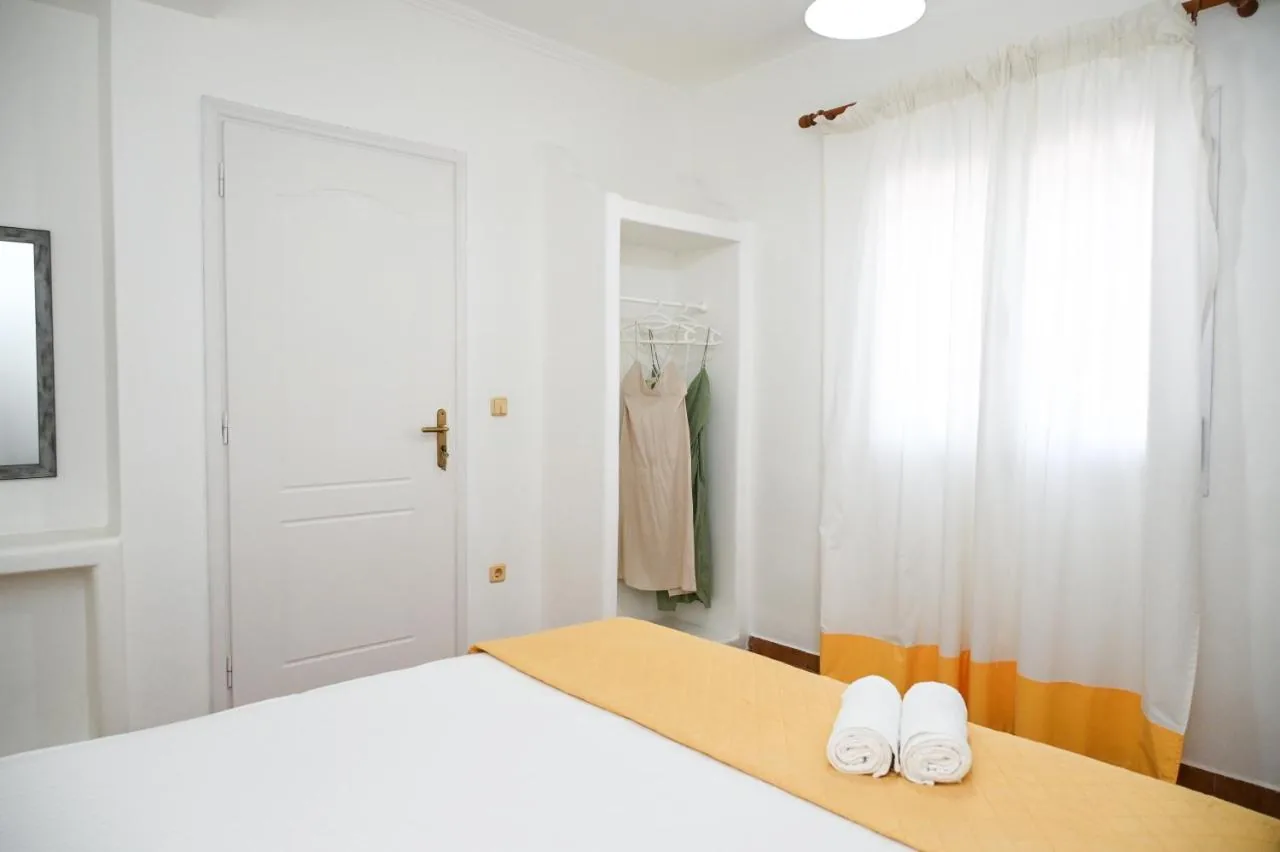 The bedroom of Navis Apartment: white walls, a mustard bedspread, folded towels, a painted sun above